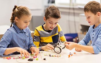 2 boys and a girl building a robotic vehicle on the table