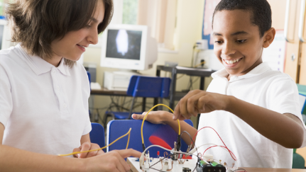 Boy and girl playing with wires attached to circuit board on a desk